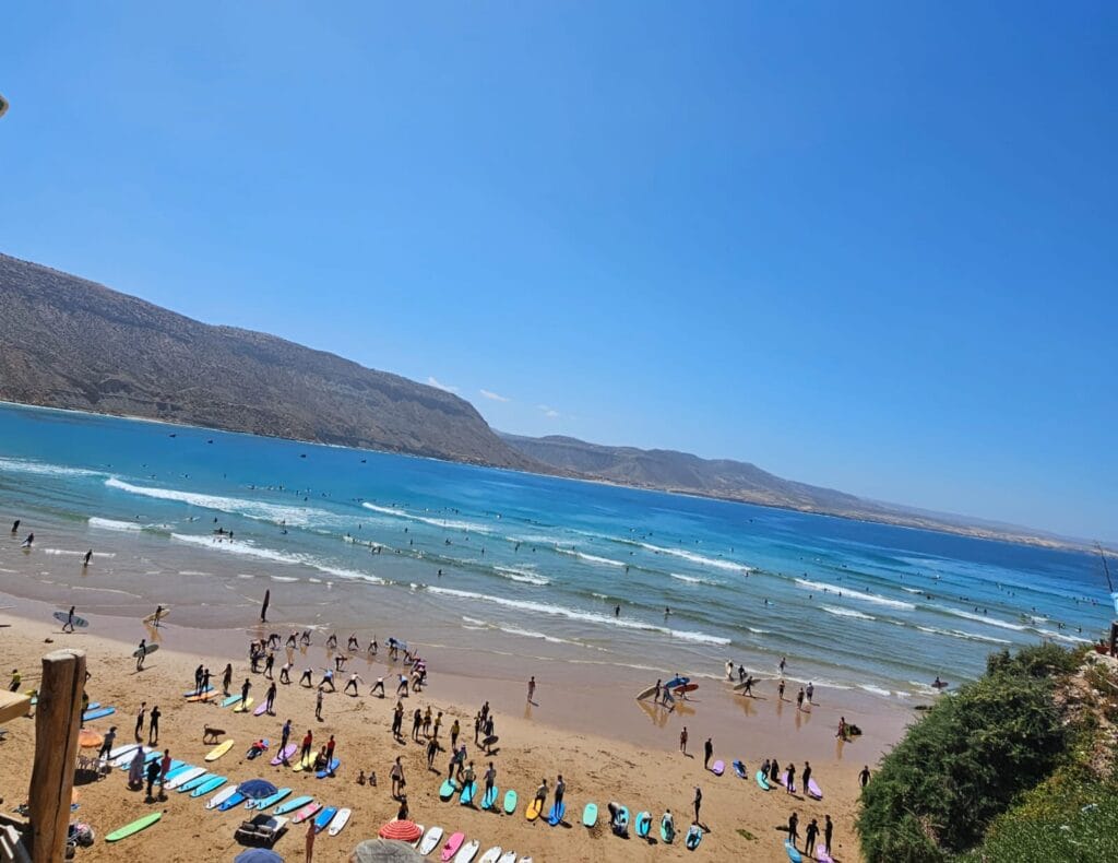 A breathtaking view of Imsouane Morocco bay from the cliff, with many surfers enjoying the surf Imsouane waves in the sparkling blue water below