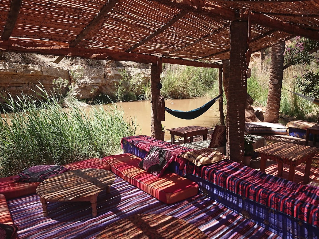 A peaceful shaded seating area with a wooden table overlooking the rocky water pools in Paradise Valley, surrounded by stunning natural views of palm trees and rocks